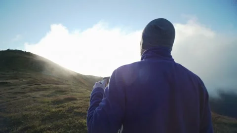 A man drinks tea and looks at the top of the mountain, the morning sun rises Stock Footage 236053179