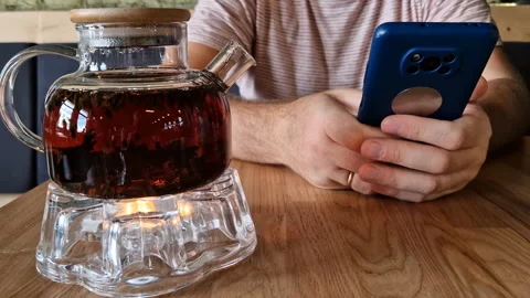 A man drinks tea and uses a mobile phone app for online business communication. Stock Footage 243256368
