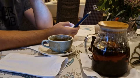 A man drinks tea and uses a mobile phone app for online business communication. Video stock 244634881