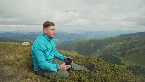 A man drinks tea or coffee from a thermos and looks at the mountain landscape Stock Footage 217395657