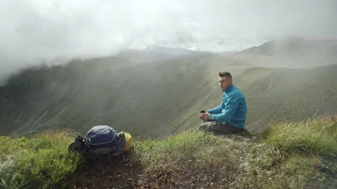 A man drinks tea from a thermos on top of a mountain in sunny weather Stock Footage 238741266