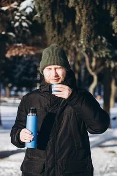 A man drinks tea while walking in the park on a sunny winter day. Stock Photos
