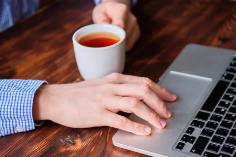 A man drinks tea while working behind a laptop. The concept of rest while wor Stock Photos