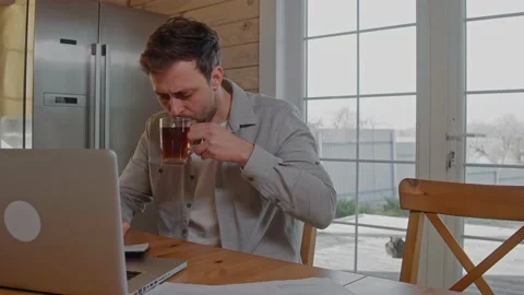 Man drinks tea working at the laptop at home because of covid restrictions Stock Footage 165411817