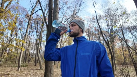 Man drinks water from a bottle in autumn forest, shot from distant to close view Stock Footage 316837994