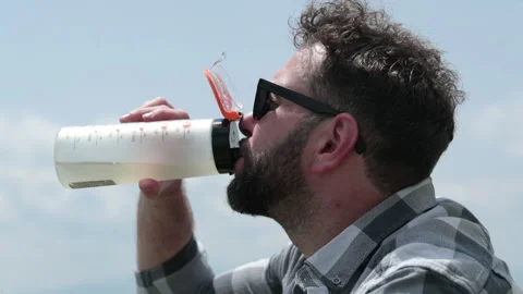 A man drinks water from a bottle while sitting on a rocky slope. Stock Footage 249215829