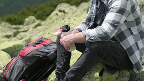 A man drinks water from a bottle while sitting on a rocky slope. Stock Footage 249215887