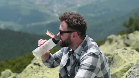 A man drinks water from a bottle while sitting on a rocky slope. Stock Footage 249215889