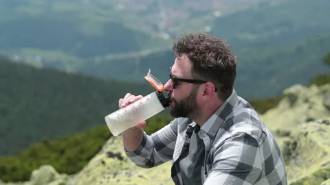 A man drinks water from a bottle while sitting on a rocky slope. Stock Footage 249215931