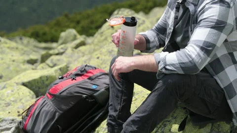 A man drinks water from a bottle while sitting on a rocky slope. Stock Footage 249215939