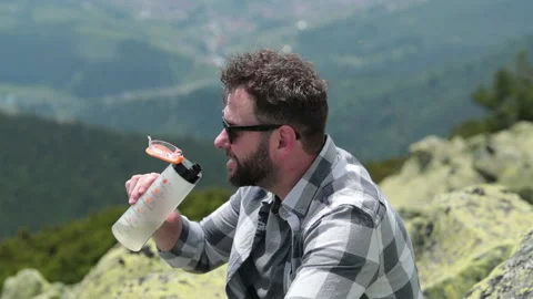 A man drinks water from a bottle while sitting on a rocky slope. Stock Footage 249215971