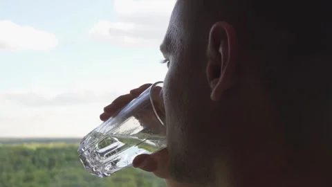 A man drinks water from a glass while looking out the window. Stock Footage 219551515