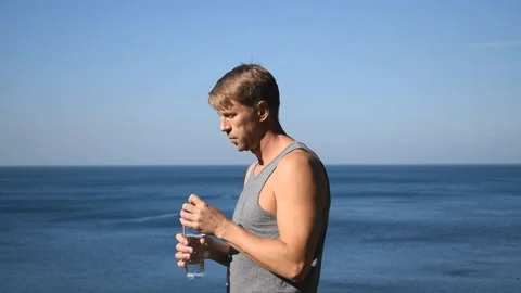 A man drinks water from a plastic bottle on the ocean, quenching thirst after ex 動画素材 96489148