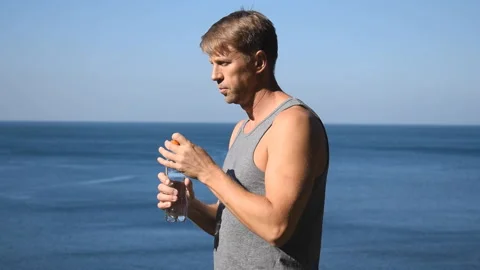 A man drinks water from a plastic bottle on the ocean, quenching thirst after ex 動画素材 96489164