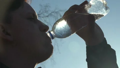 A Man Drinks Water from a transparent Plastic Bottle against a Blue Sky. Close Stock Footage 152888584