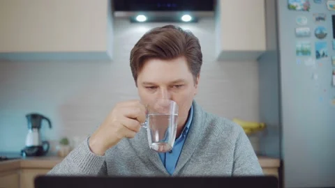 Man drinks water while working at a laptop Stock Footage 148817748