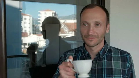 A man drinks from a white cup and looks at the city through a window. Stock Footage 79577605