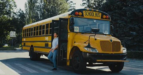 Man driver coming out schoolbus cabin. Empty school bus standing on parking lot. Stockfoto's