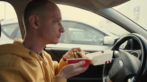 Man driver sit in a car hold eat a big meat burger from mcdrive bite it and chew Stock Footage 142632759