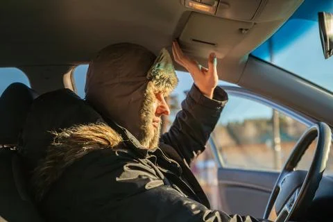 Man driver in a warm fur hat blocking sun with visor in car Stock Photos