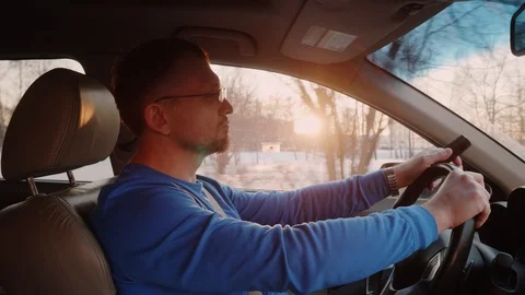Man drives car car with button phone in hand. Sunset and sun beams through trees Stock Footage 109436327