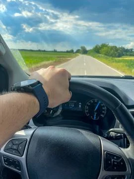 A man drives a car down an open rural road under a partly cloudy sky. Stock Photos