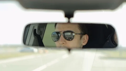 A man drives a car. Reflection face in the rearview mirror of the automobile. Stock Footage 73998766