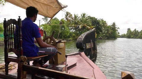 A man drives a houseboat through the backwaters of Kerala, India. Stock Footage 83595124