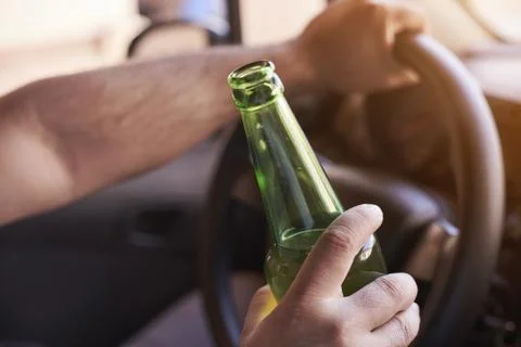 A man driving a car while holding a bottle of beer. Drunk diving, unsafe driv Stock Photos