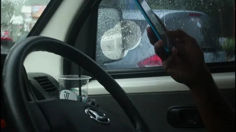 A man is driving a car while playing on his cellphone when it rains. Stock Footage 266683136