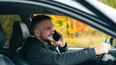 A Man Driving a Car While Talking on His Smartphone on a Sunny Autumn Day Wit Stock Photos