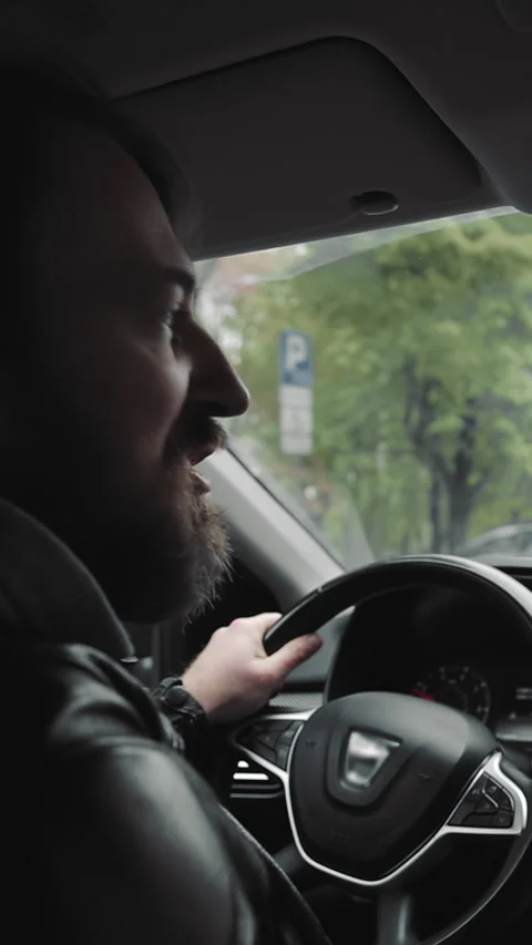 Man driving car while using hands-free phone. A man in a leather jacket drives a Stock Footage 317890475