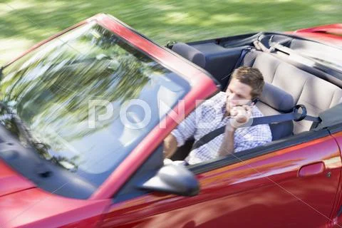 Man driving convertible car using cellular phone and smiling Stock Photos