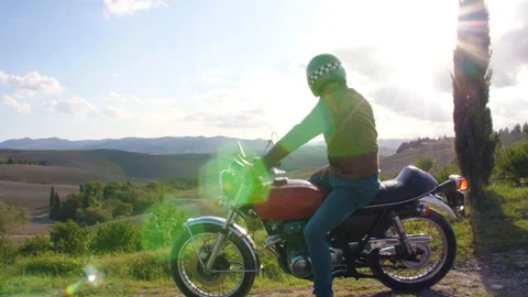 Man driving a red motorcycle at sunset on road in beautiful hills landscape in Stock Footage 239028193