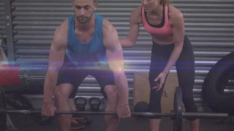 Man driving through legs lifting barbell while woman coach correcting posture Stock Footage 323386119