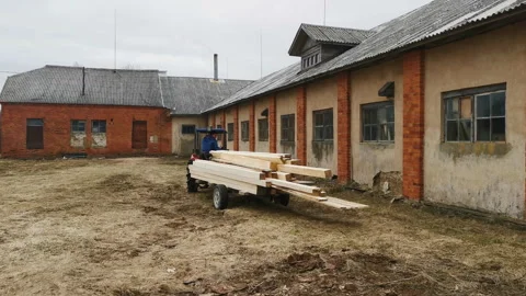 Man driving tractor with sawed planks stacked on a trailer behind next to 스톡 동영상 272446387