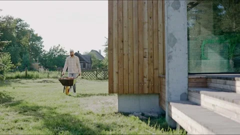 Man is driving a wheelbarrow working at the backyard on a sunny day. Stock Footage 199871374