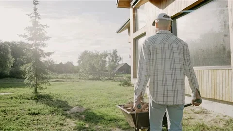 Man is driving a wheelbarrow working at the backyard on a sunny day. Video stock 199871549