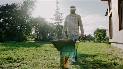 Man is driving a wheelbarrow working at the backyard on a sunny day. 스톡 동영상 199871814