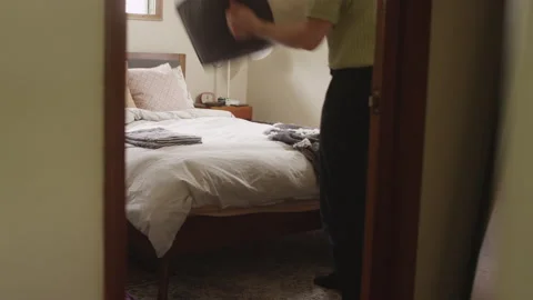 Man dumps a laundry basket of clothes onto a bed to get ready to fold them Video stock 134286962