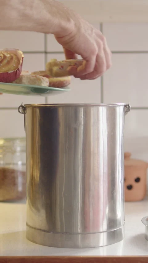 Man dumps stale donuts on plate into metal food waste bin in kitchen, vertical Stock Footage 297465314