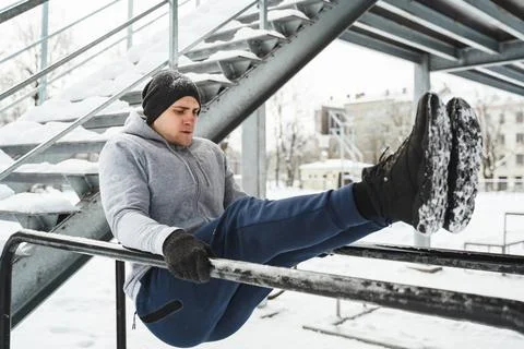 Man during calisthenics workout on a parallel bars during snowy winter day... Foto stock