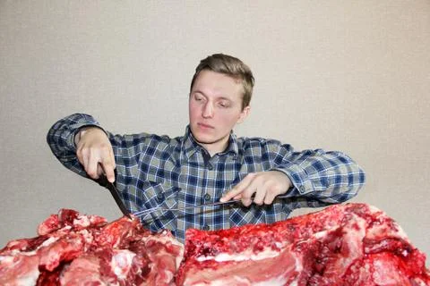 A man eagerly looks at raw meat. A man with a knife and a fork Stock Photos