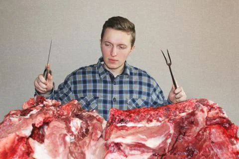 A man eagerly looks at raw meat. A man with a knife and a fork. A lot of fres Stock Photos
