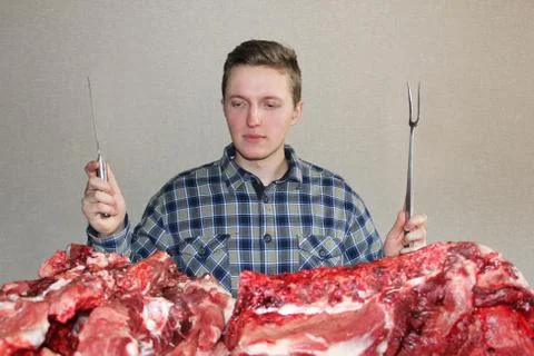 A man eagerly looks at raw meat. A man with a knife and a fork. A lot of fres Stock Photos