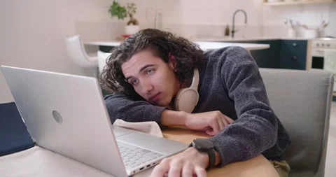 Man early 20s dozing at kitchen nook, noticing laptop screen, lifting head, Stock Footage 341027194