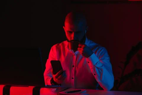 A man with earphones is working remotely in the rays of blue and red light. Stock Photos