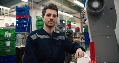 A man with an earring and in a blue uniform poses near a sewing machine in a Stock Footage 244477703