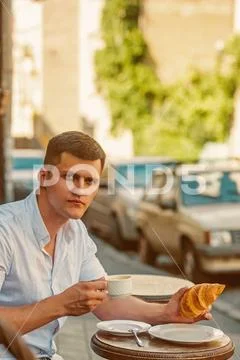 Man eat and drink coffee in street cafe. Macho enjoy cup of tea and croissant on Stock Photos