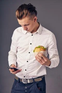 Man eat hamburger in cafe while watch video on his phone Stock Photos